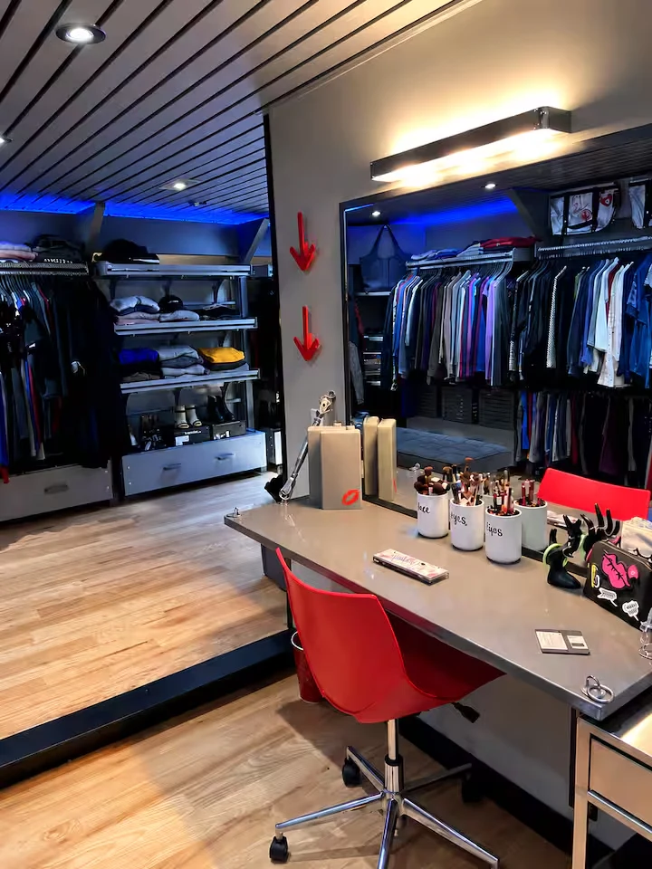 Makeup station with red chair, wide mirror, illuminated vanity and dressing-room shelving