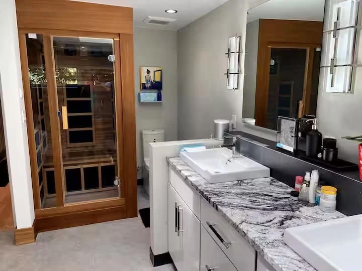 Primary bathroom vanity with patterned countertop, large mirror and private infrared sauna