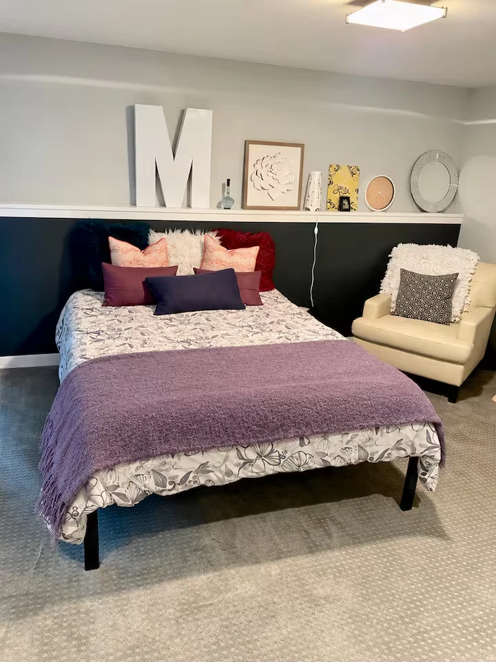 Guest bedroom with floral bedding, purple throw, cream lounge chair and artwork on a display ledge