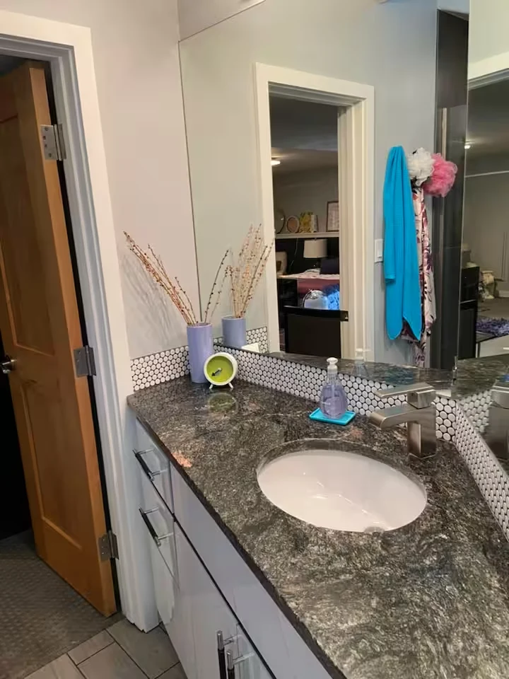 En-suite bathroom vanity with stone countertop, oval sink, large mirror and view into bedroom