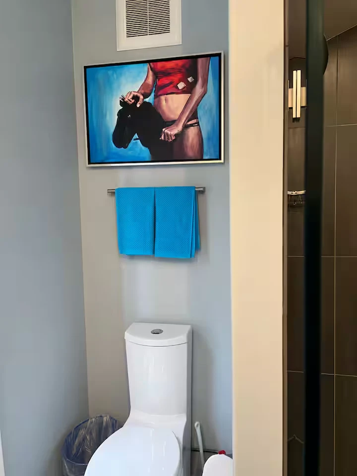 Guest bathroom with framed artwork, turquoise towels, white toilet and glass shower entrance