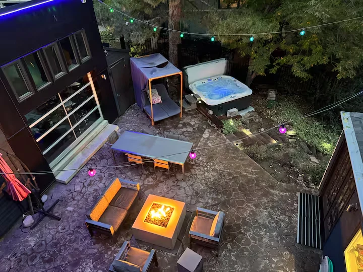 Overhead courtyard view with hot tub, covered lounge, dining table, fire pit and colorful string lights
