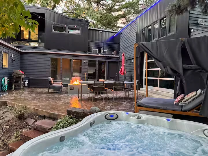 Bubbling hot tub in the foreground with courtyard seating, fire pit and dark residence exterior behind