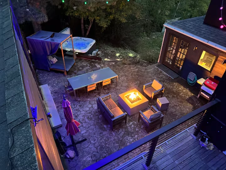 Elevated view of courtyard seating around a lit fire pit, hot tub and outdoor dining area at dusk