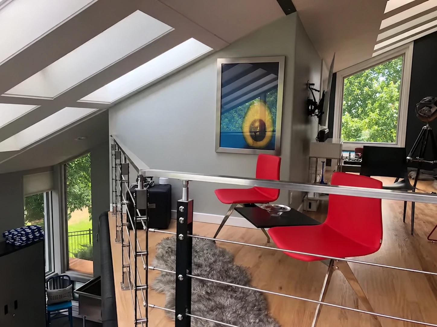 Elevated sitting area with red chairs, small table, framed artwork and steel railing beneath skylights