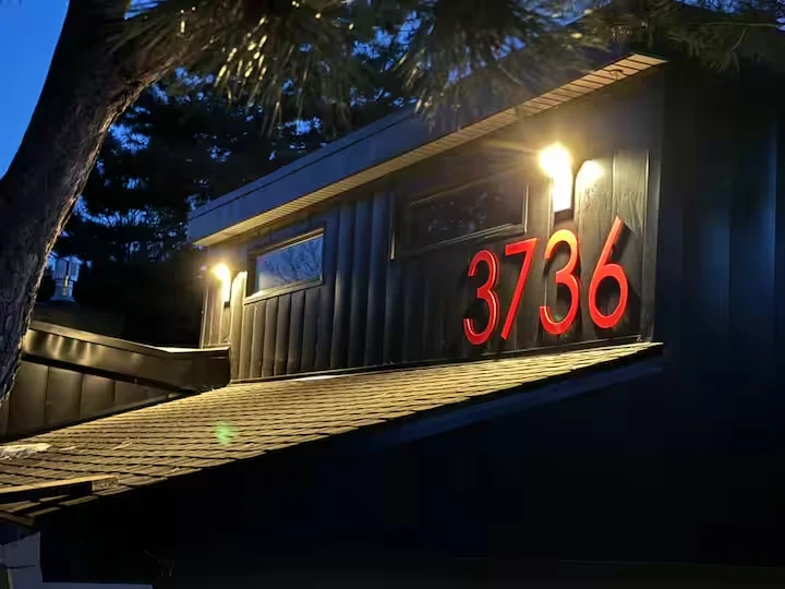 Illuminated red address signage on the dark exterior beneath tree branches at dusk