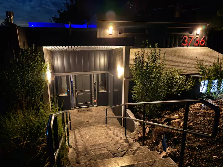 Illuminated private entrance at night with stone steps, metal handrails and surrounding landscaping