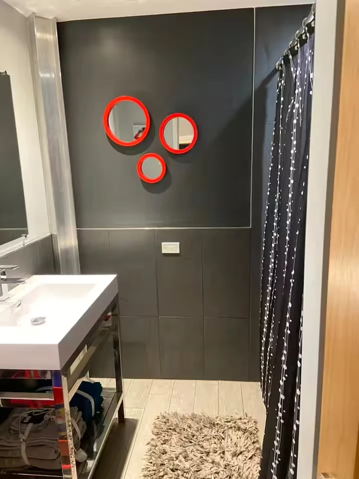 Guest bathroom with charcoal walls, red circular mirrors, white sink and dark patterned shower curtain