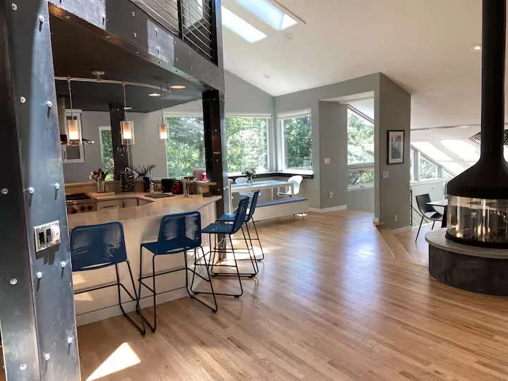 Kitchen breakfast bar with blue stools beneath steel beams, beside the open living area