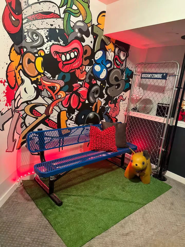 Gaming area with colorful street-art mural, blue metal bench, red accent lighting and green turf rug