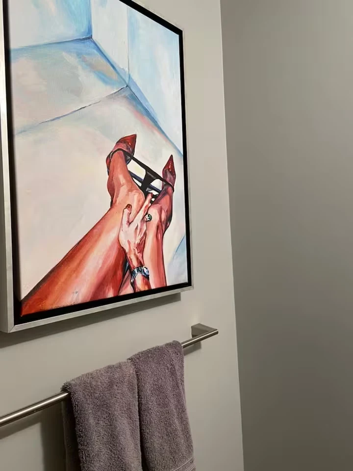 Framed contemporary artwork above a metal towel rail with a purple hand towel in the powder room