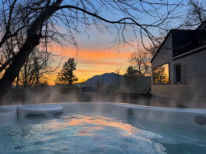 Steam rising from the hot tub at sunset with orange sky, mountain silhouette and the residence beside it