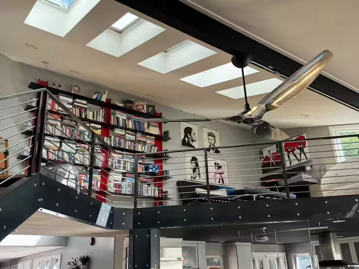 Elevated library with tall red-and-black bookshelves, portrait artwork, steel railing and skylights