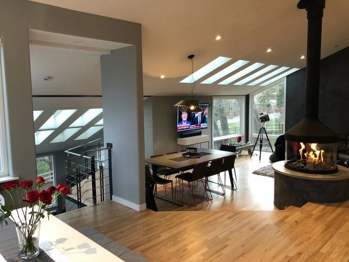 Open living and dining space with a lit circular fireplace, skylights and steel stair railing