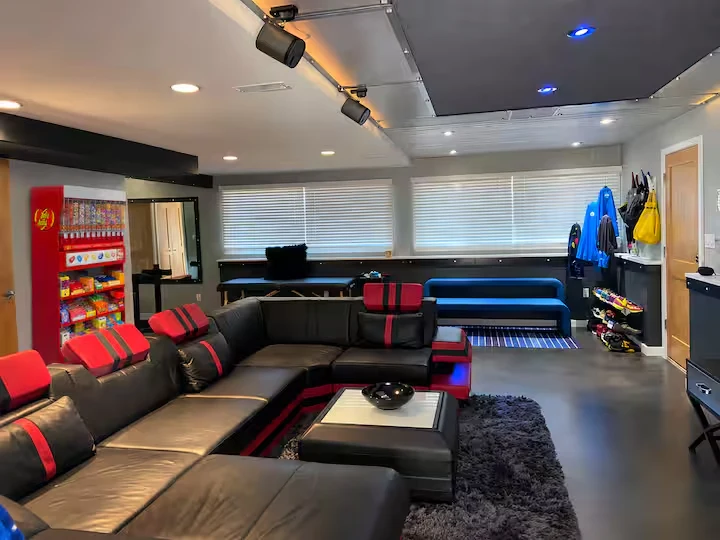 Wide cinema lounge view with oversized black sectional, red headrests, candy station and blue bench