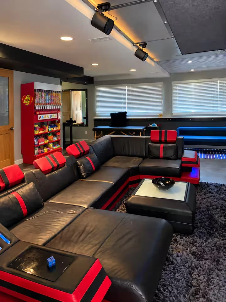 Black leather cinema sectional with red accents beneath track lights beside the candy dispenser